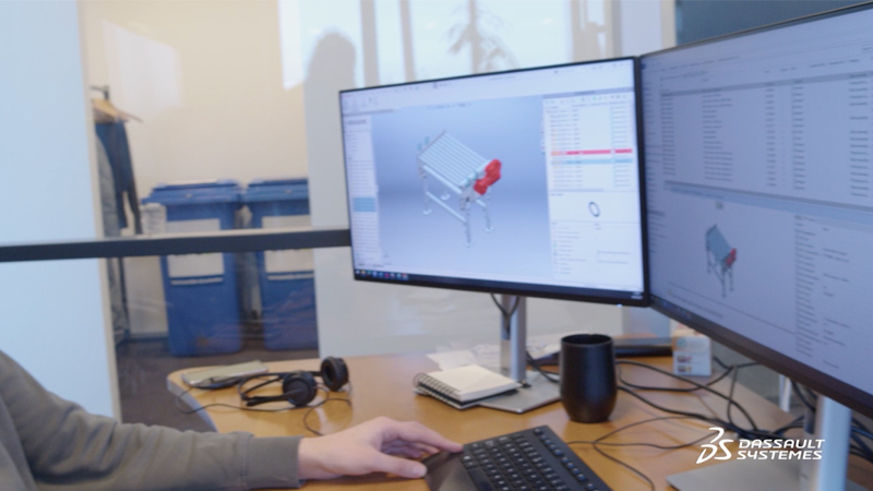 Person looking at two monitors showing SOLIDWORKS 3D model of an assembly with related data