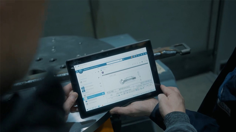 Worker on shop floor looking at tablet showing SOLIDWORKS drawing of a part