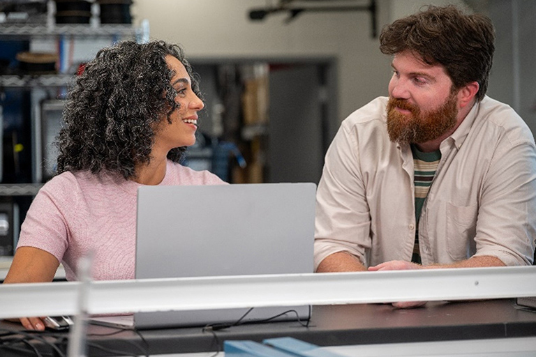 Two people talking in an office. One person has a laptop.