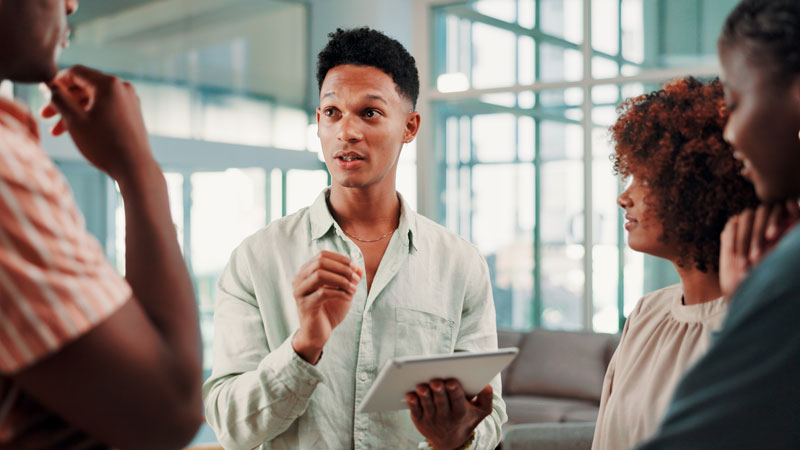 Man holding a tablet and talking to three others